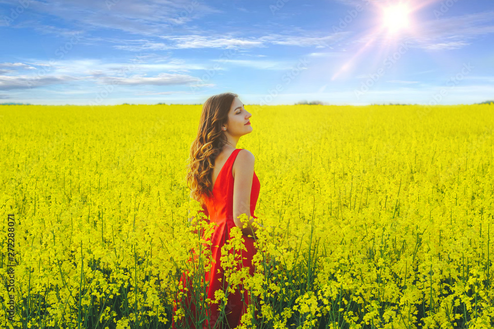 Young beautiful girl in a red dress close up in the middle of yellow field with radish flowers and sunlight.. Young beautiful girl in a red dress close up in the middle of yellow field with radish flowers and sunlight..