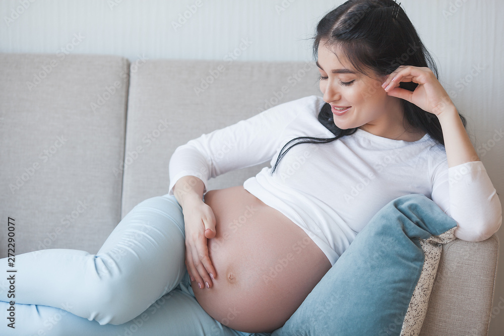 Attractive young woman expecting a child. Pregnant woman. Female indoors embracing her stomach. Attractive young woman expecting a child. Pregnant woman. Female indoors embracing her stomach.