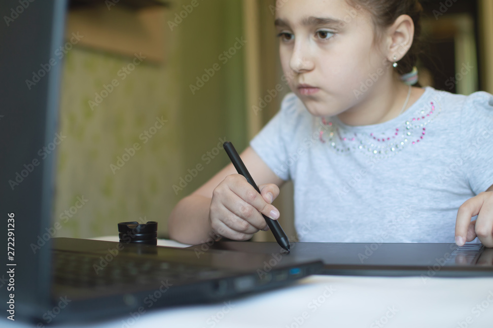 child girl draws on a graphic tablet while sitting at a table with a laptop child girl draws on a graphic tablet while sitting at a table with a laptop