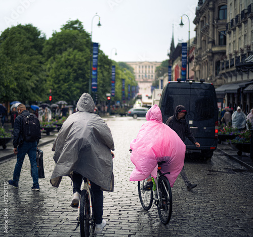 Couple cycling in Oslo's main streat wearing plastic rain ponchos