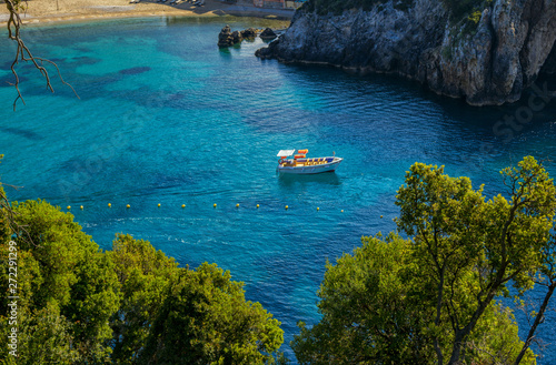 Beautiful landscape with sea and small boat on a water surface, beach, mountains and cliffs, green trees and bushes, rocks in a blue water. Corfu Island, Greece. 