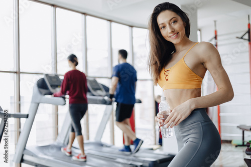 Fototapeta Naklejka Na Ścianę i Meble -  young attractive girl in the gym drinking water on the background of treadmills