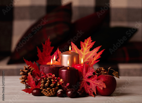 Autumn still life - candles, leaves and cones on the background of pillows.