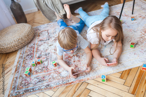 Little cute kids playing smartphone. Brother and sister at home playing video games.