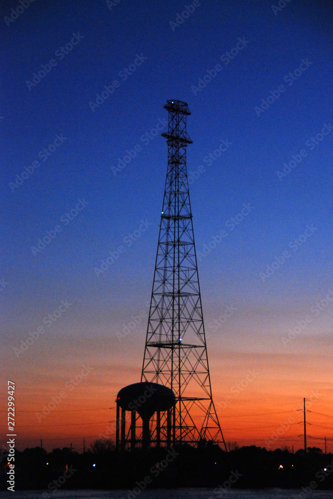 oil production tower against dark blue and orange sky at sunset
