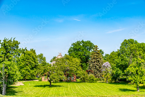 You see a landscape in Lower Saxony with green meadows. Almost hidden from trees stands a typical house for this region.