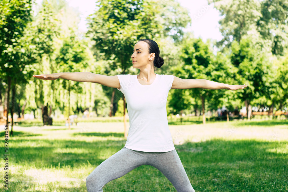 Beautiful young woman doing yoga at park and looking away. Brunette woman enjoying nature during a breathing exercise. Beautiful young woman doing yoga at park and looking away. Brunette woman enjoying nature during a breathing exercise.