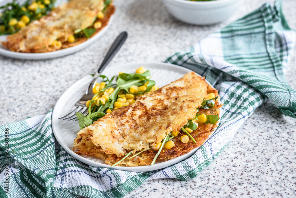 Potato rosti with corn and rocket salad served on a gray background. Traditional swiss dish Potato rosti with corn and rocket salad served on a gray background. Traditional swiss dish