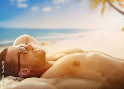 Handsome, muscular man relaxing on a tropical beach photo