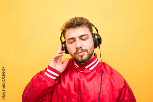 Close-up portrait of an adult man listens to music in headphones with closed eyes on a yellow background. Music enthusiast enjoys music. Isolated