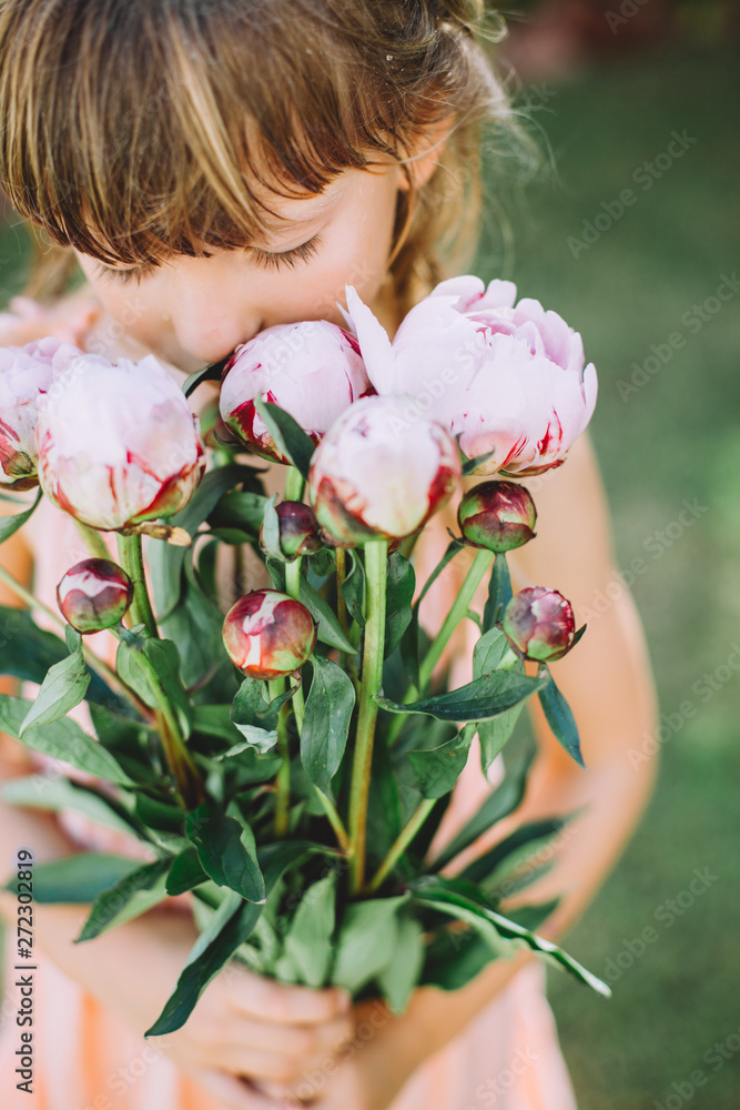 Little cute girl holding a bouquet with pink peonies
