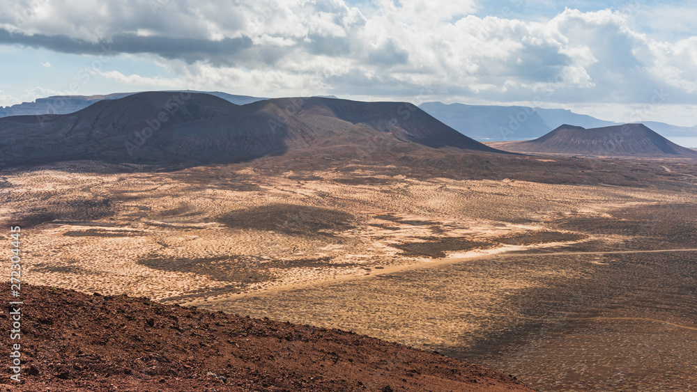 View over the vast deserted volcanic landscape of the Island of La Graciosa in Canary, Spain, with volcano crater silhouettes in the distance. Scenic mars like background.