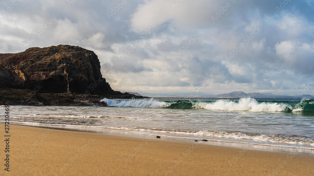 Waves washing the white sand of the untouched Wax Beach (Playa de la Cera) in a scenic frame of turquoise water and black volcanic rugged cliffs. Seascape in Lanzarote, Canary, Spain. Waves washing the white sand of the untouched Wax Beach (Playa de la Cera) in a scenic frame of turquoise water and black volcanic rugged cliffs. Seascape in Lanzarote, Canary, Spain.