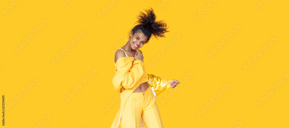 Playful happy young african woman wear stylish yellow clothes look at camera dancing funky black teen fashion girl on summer studio background, horizontal banner header website design, copy space