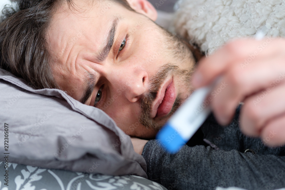 A sick man looks at a thermometer A sick man looks at a thermometer