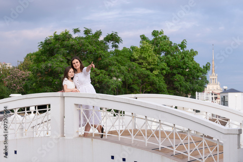 Family on vacation at the hotel. Mom shows her daughter the sights. Girls dressed in white dresses are on the bridge. © Aleksandr