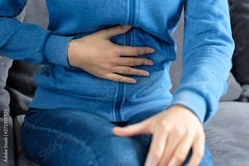 A girl holds her hand on a sore stomach while sitting at home on the couch