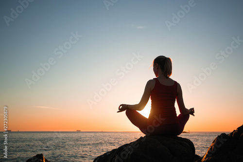 Silhouette of yoga woman on the ocean coast during soft warm sunset.