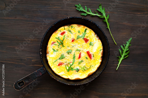 Freshly cooked omelet with herbs and tomatoes on rustic metal pan.