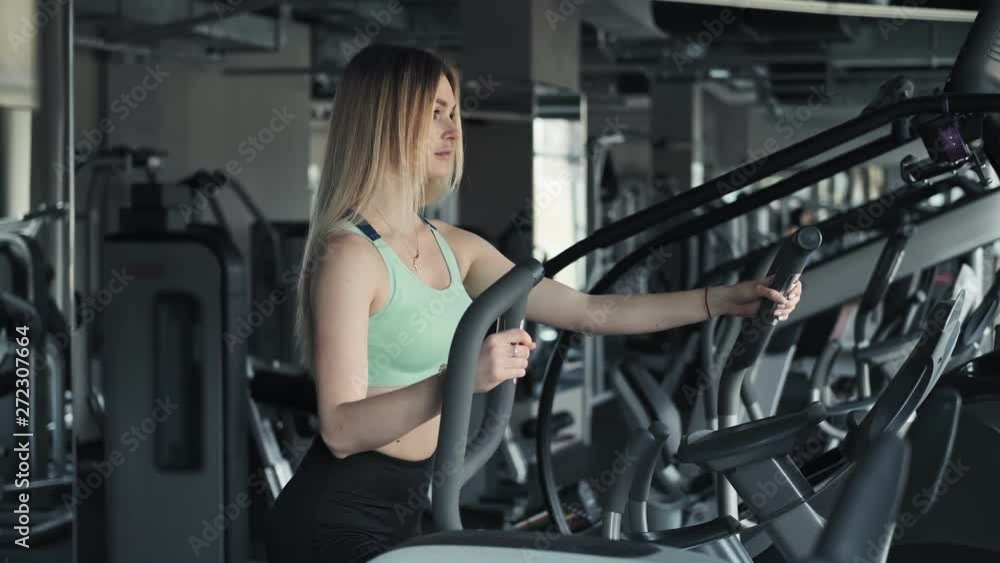 Young woman during cardio workout on an elliptical trainer. Fit blonde woman training in gym. Medium shot Young woman during cardio workout on an elliptical trainer. Fit blonde woman training in gym. Medium shot