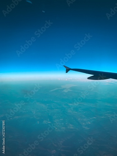 View out of a airplane window with a aerial view down to the alps with blue sky horizon and colorful sunset light and clouds. Flying over Switzerland