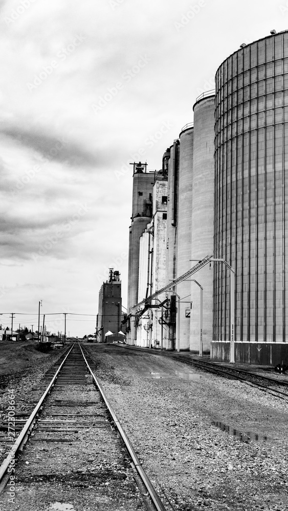 Fototapeta premium Large grain elevators with bold skies in color and black and white Railroad tracks as leading lines
