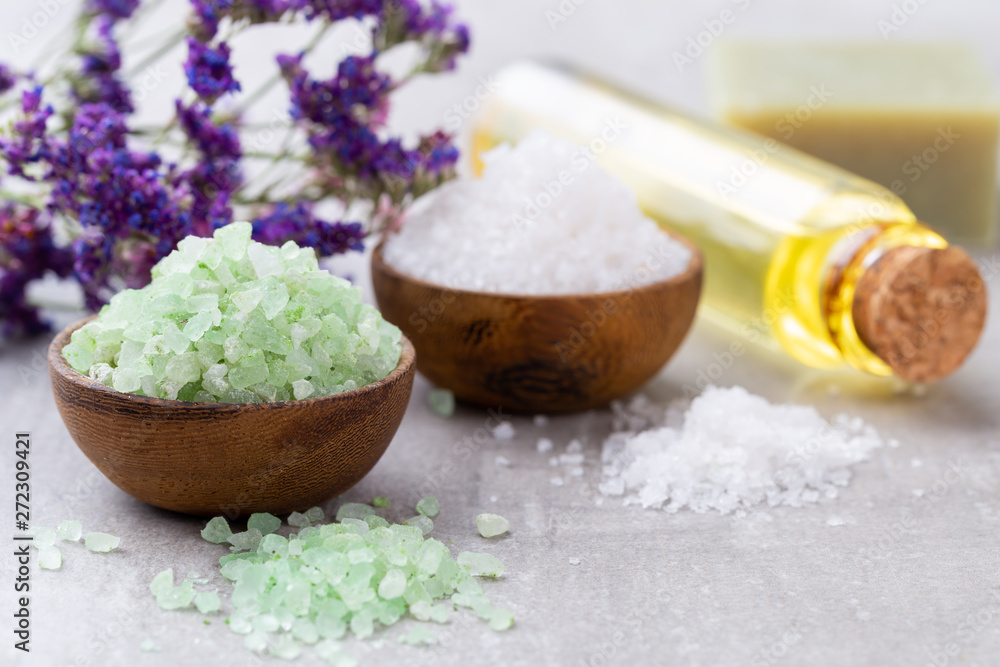 Sea salt in bowl, aroma oil in bottles, Wellness and flowers on grey textured background and flowers on vintage wooden background. Selective focus. Sea salt in bowl, aroma oil in bottles, Wellness and flowers on grey textured background and flowers on vintage wooden background. Selective focus.