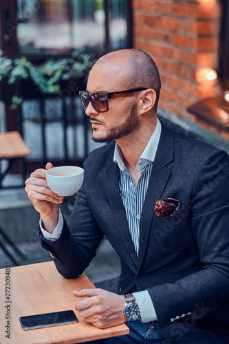 Cheerful groomed gentelman in sunglasses is enjoying his coffeebreak with cup of fresh latte.