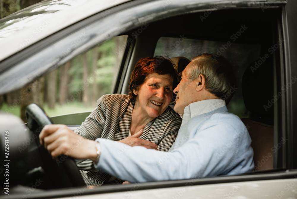 Happy elderly couple inside modern car. Seniors travelling together in car. Smiled and active retirees having date and romance inside new car. Happy aged family concept