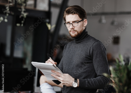 The guy dressed in casual office style clothes makes notes in a notebook in the modern office