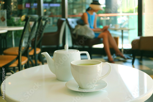 Cup of hot green tea with teapot on the white cafe's round table