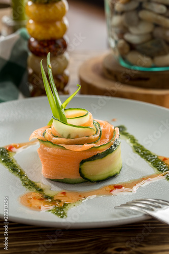 Restaurant Starter with Raw Salted Salmon Slices and Cucumber on white plate on wooden table