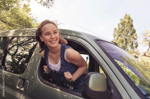 Travel, tourism. Happy Girl looks out the window of the car on a trip, enjoys traveling in a car, lifestyle, relaxation, emotional portrait with copy space, summer background