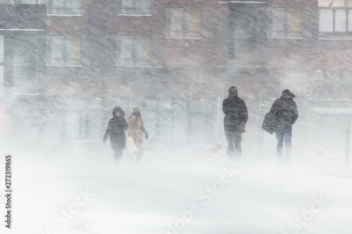 The blizzard, strong wind, sleet, against the background of houses blurred silhouettes of people, they try to hide from bad weather, overcome all difficulties of severe climate. go to the bus stop