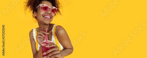 Happy young african woman holding drink wear glasses laughing, cheerful black teen girl enjoy summer detox cocktail having fun isolated on yellow studio background, banner website design, copy space