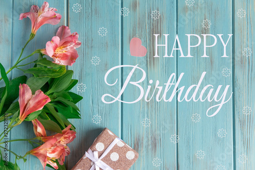 Greeting card with the inscription happy birthday. Congratulatory greeting to the girl, mother with flowers and a gift on a wooden background. Alstroemeria flowers