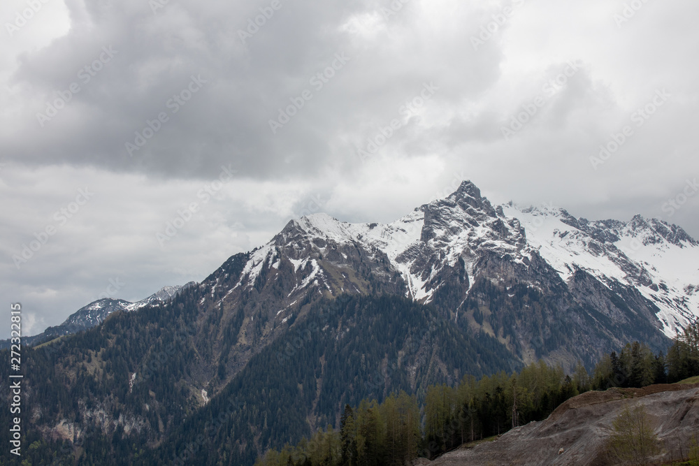 Panorama of an alpine landscape with high mountains, green meadows and trees in spring with snow in Austrian Alps