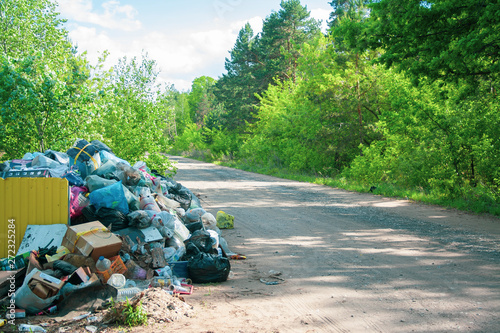 Illegal dump near the country sand road in the country on sunny day. Trash pollution in the nature. Dirty dump near the forest woods photo