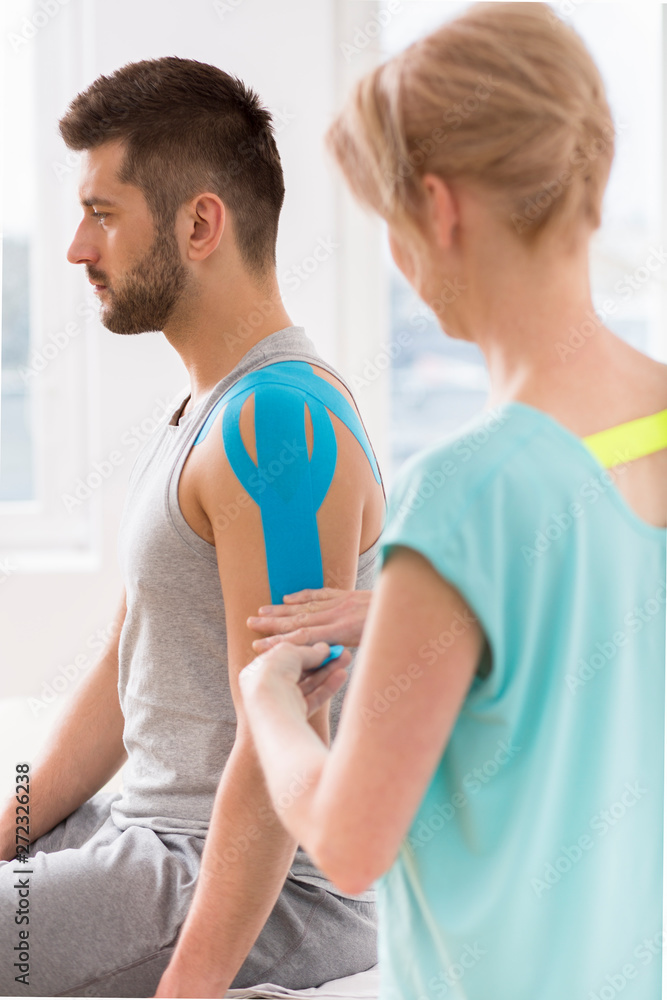 Physiotherapist covering selected fragments of young man's body with special structure patches during kinesiotaping therapy