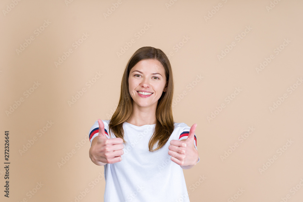 Front view of young adult woman smiling, looking at camera and showing thumb up on two hands Front view of young adult woman smiling, looking at camera and showing thumb up on two hands