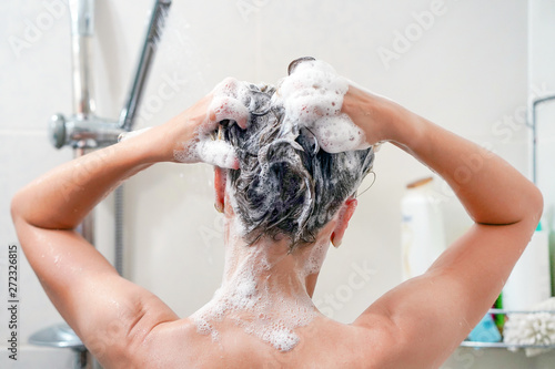 Woman washes her hair with shampoo in bathroom. Woman washing her hair with a lot of foam inside a shower. Back view of young woman washing her hair. Close-up.