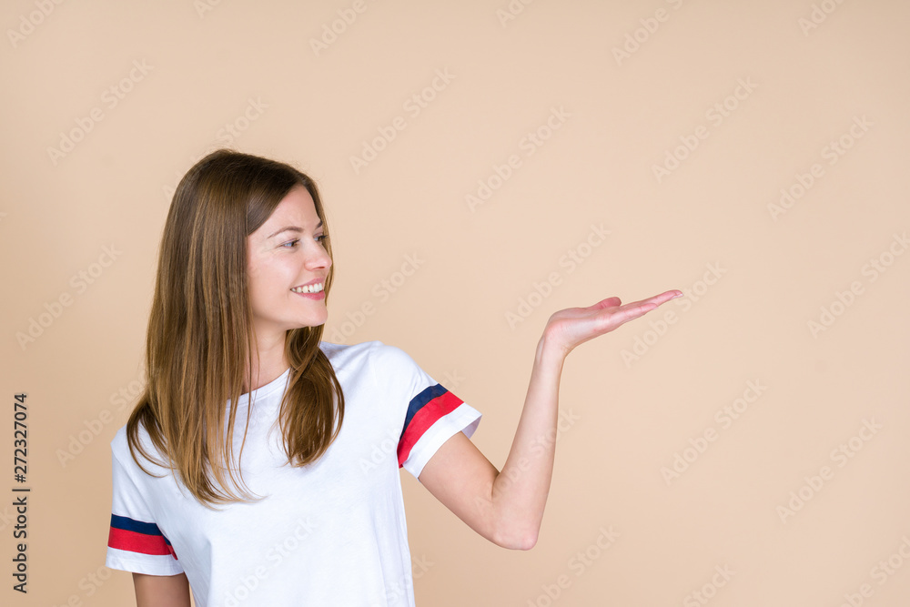 Front view of young adult woman looking aside and holding invisible object on palm hand Front view of young adult woman looking aside and holding invisible object on palm hand