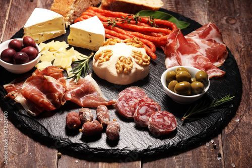 Cutting board with prosciutto, salami, cheese,bread and olives on dark stone background
