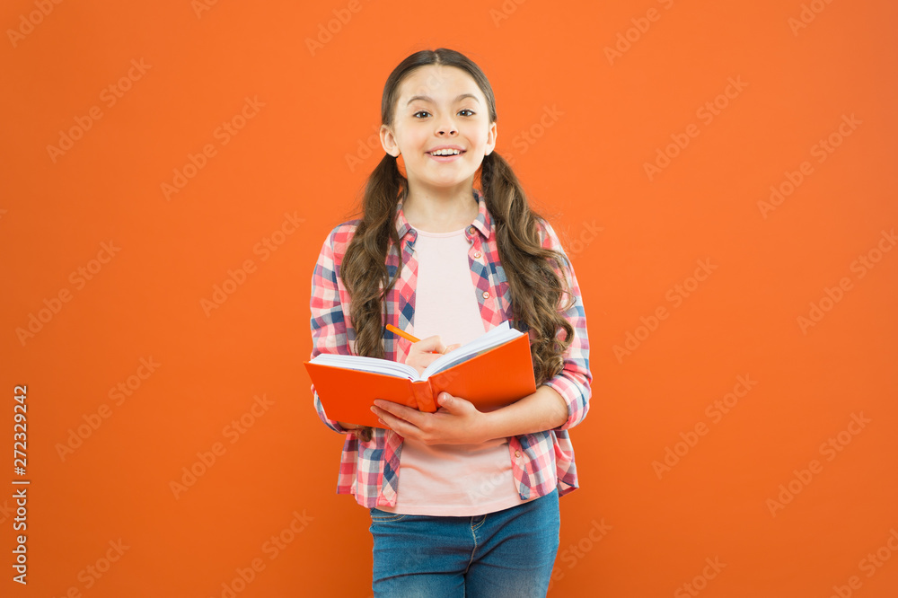 Dig into reading. Cute small child reading a book on orange background. Adorable little girl learn reading and writing. Home reading and schooling Dig into reading. Cute small child reading a book on orange background. Adorable little girl learn reading and writing. Home reading and schooling