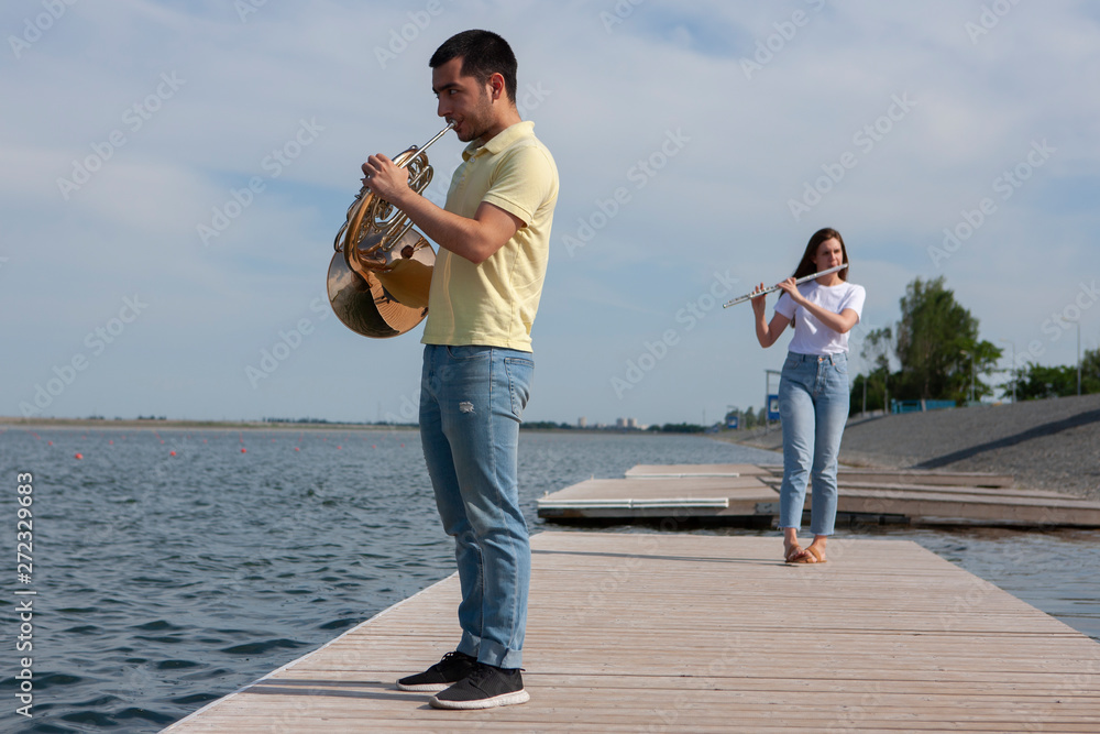 The guy playing the horn and the girl playing the flute on the lake The guy playing the horn and the girl playing the flute on the lake