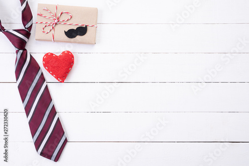 Happy fathers day concept. Top view of blue tie, beautiful gift box, red heart with man mustache on white wooden table background. Flat lay.