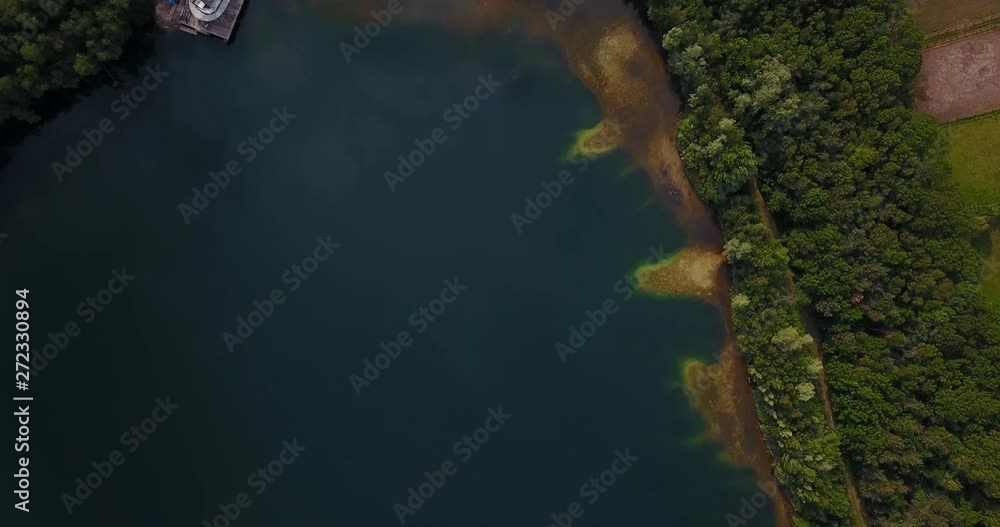 Top down aerial drone shot while drone loses height showing an unspoiled environment with a beautiful blue lake with rich green vegetation at it's shore. Top down aerial drone shot while drone loses height showing an unspoiled environment with a beautiful blue lake with rich green vegetation at it's shore.