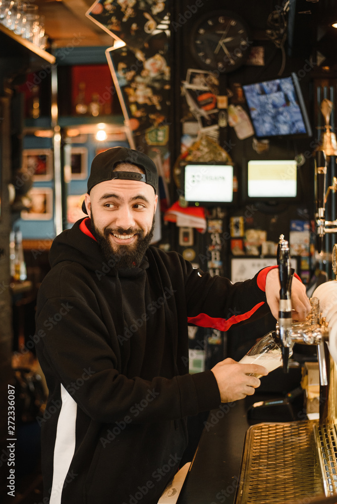 smiling barman pouring beer in a bar. Bearded courageous man pours you a foaming drink.