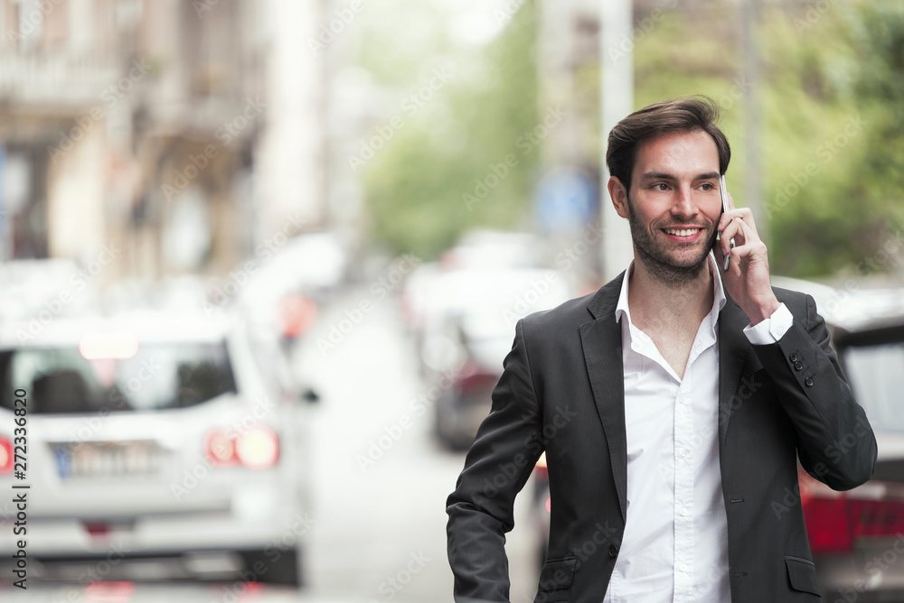 Cheerful happy young business man enjoying a nice talk over his phone, walking the streets of a city
