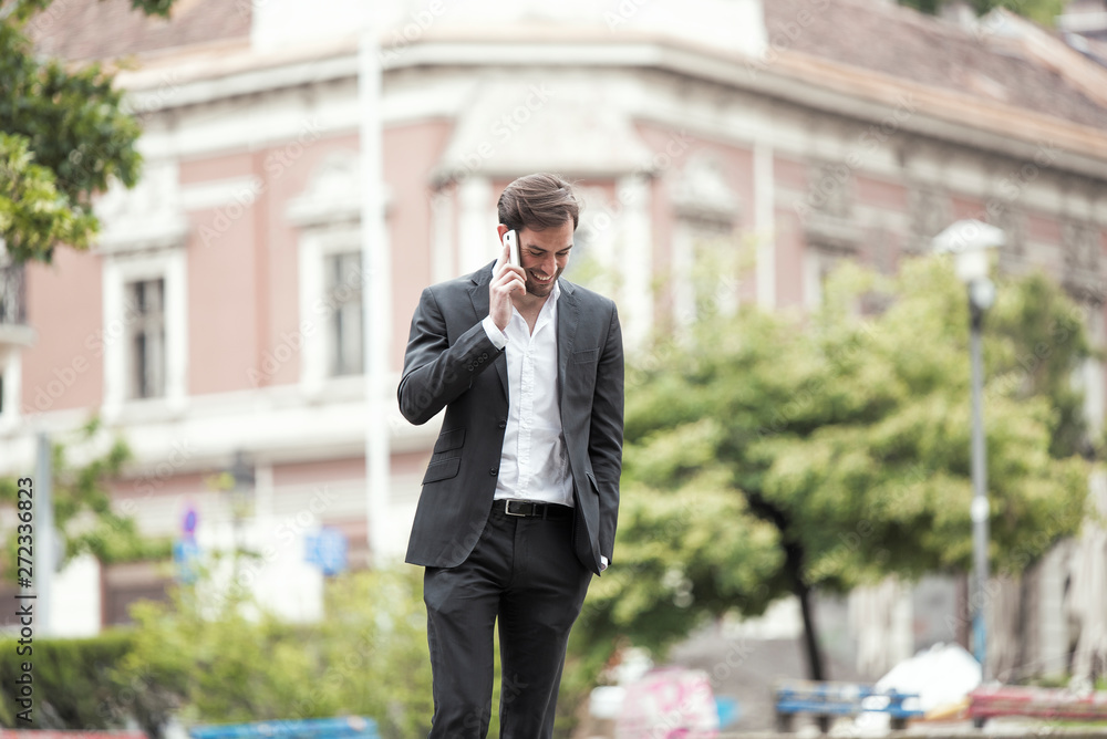 Cheerful happy young business man enjoying a nice talk over his phone, walking the streets of a city Cheerful happy young business man enjoying a nice talk over his phone, walking the streets of a city